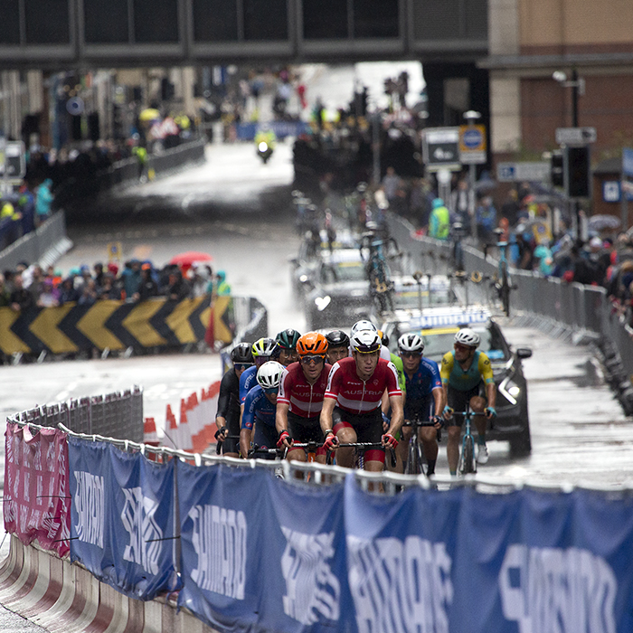 2023 UCI Cycling World Championships - Road Race - Elite Men - A group of riders on Cathedral Street followed by the race convoy