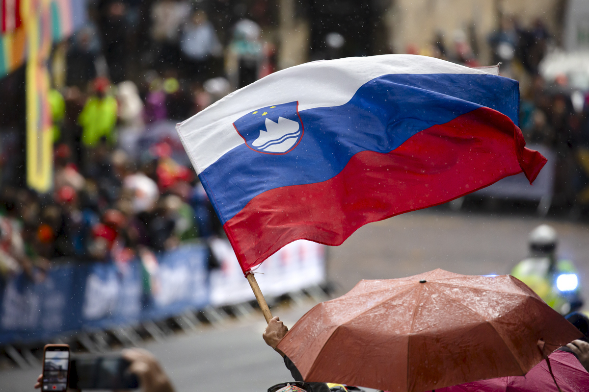 2023 UCI Cycling World Championships - Road Race - Elite Men - Spectators shelter under umbrellas as one fan waves the flag of Slovenia 