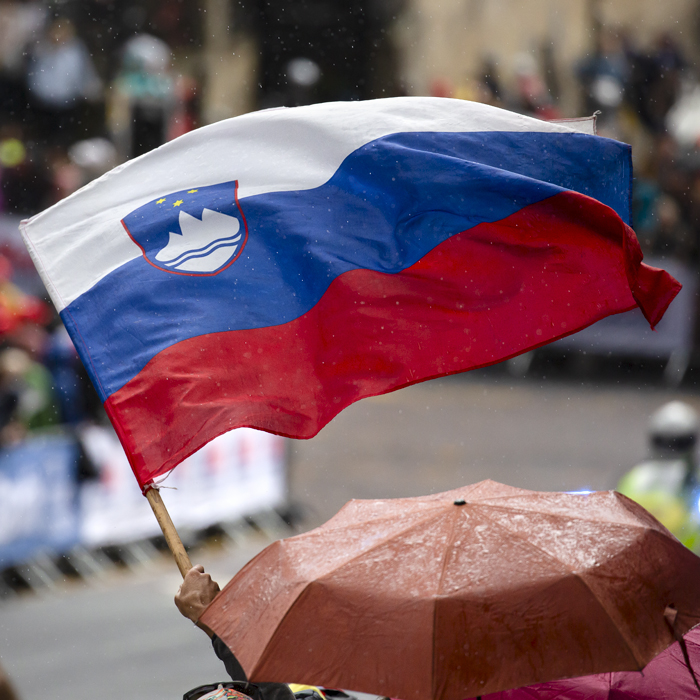 2023 UCI Cycling World Championships - Road Race - Elite Men - Spectators shelter under umbrellas as one fan waves the flag of Slovenia 