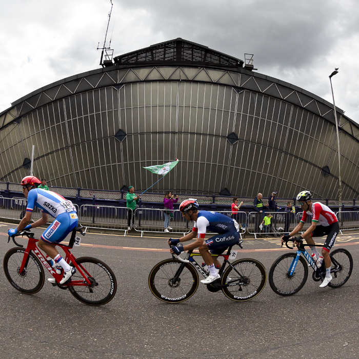 2023 UCI Cycling World Championships - Road Race - Elite Men - A group of riders pass the glass arch of Glasgow Queen Street Station while a fan waves a flag in the background