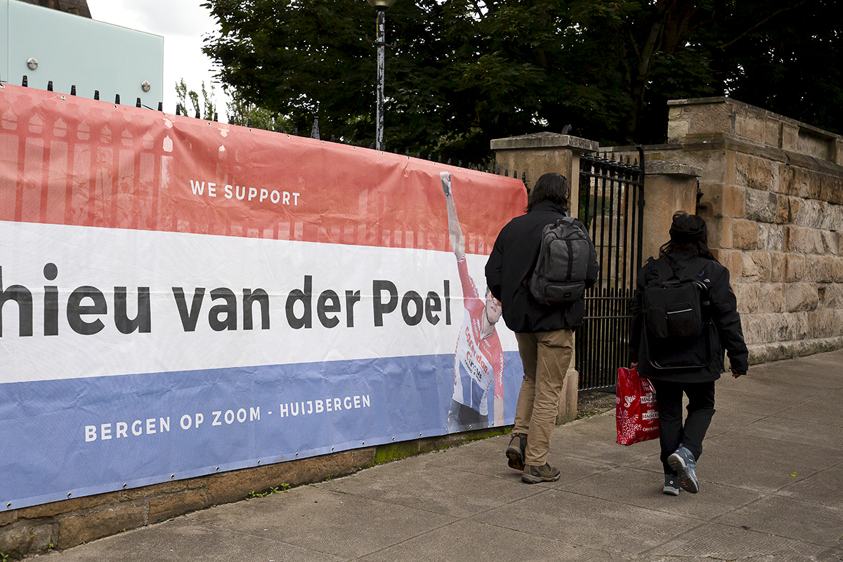 2023 UCI Cycling World Championships - Road Race - Elite Men - Two people walk past a giant banner hung from railings dedicated to Mathieu van der Poel of the Netherlands