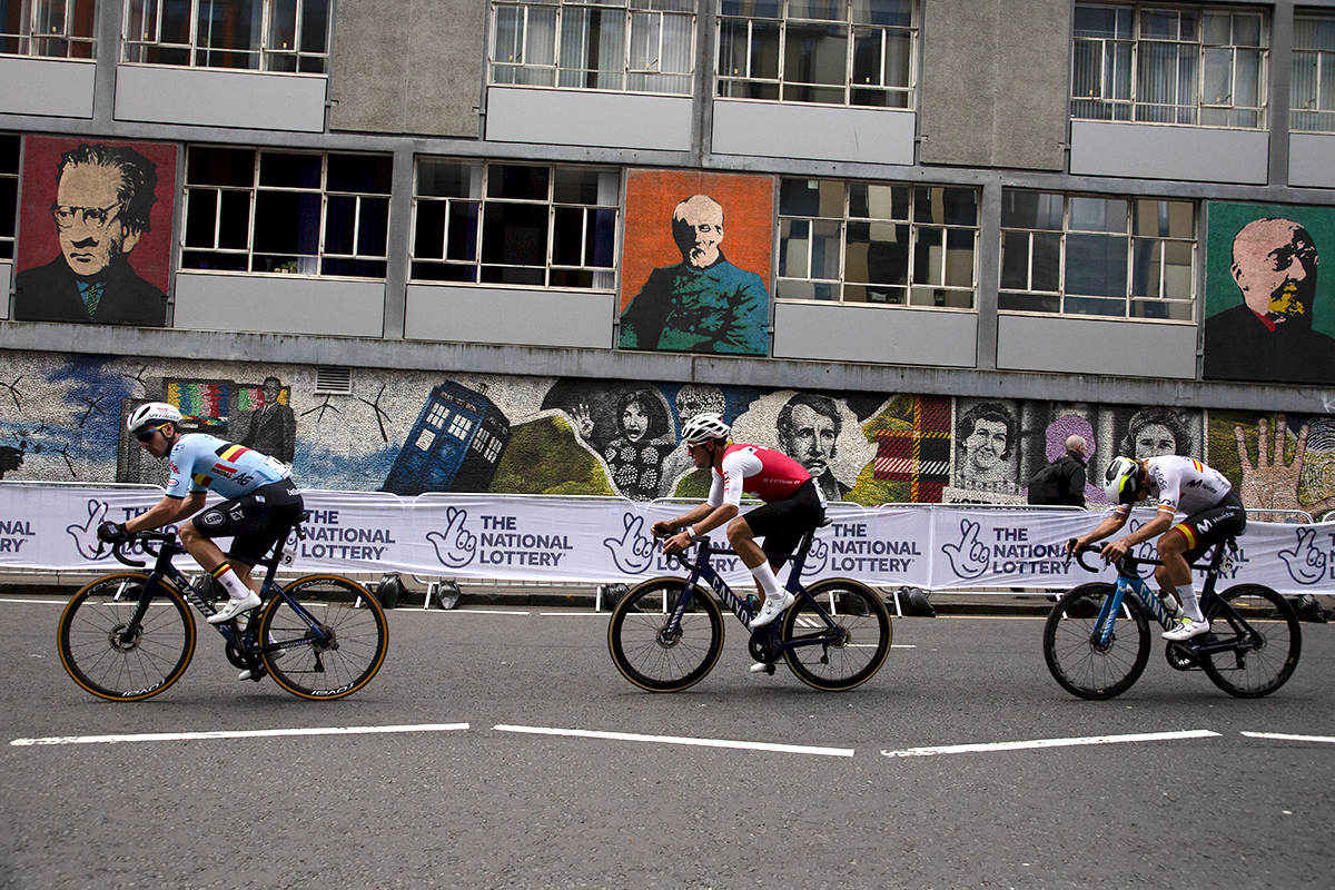 2023 UCI Cycling World Championships - Road Race - Elite Men - Riders pass a mural showing famous alumni of the University of Strathclyde