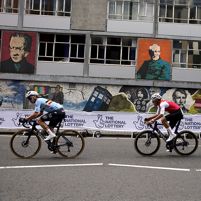 2023 UCI Cycling World Championships - Road Race - Elite Men - Riders pass a mural showing famous alumni of the University of Strathclyde