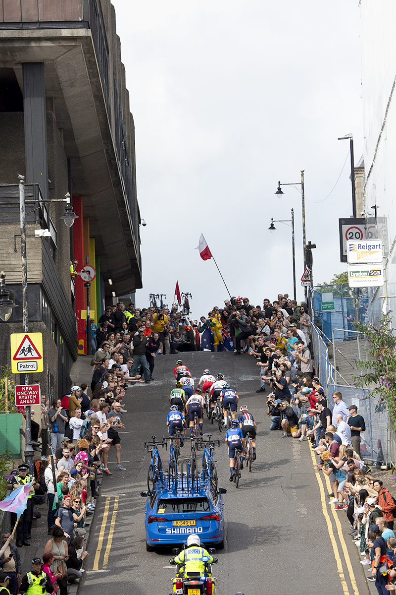 2023 UCI Cycling World Championships - Road Race - Elite Women - A group of riders climb the steep hill of Scott Street followed by a race vehicle