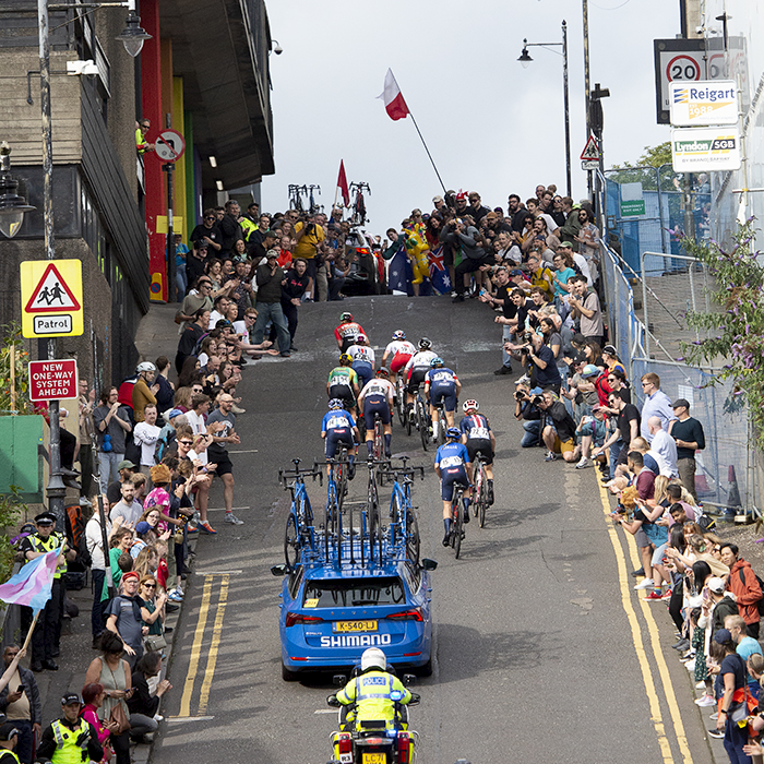 2023 UCI Cycling World Championships - Road Race - Elite Women - A group of riders climb the steep hill of Scott Street followed by a race vehicle