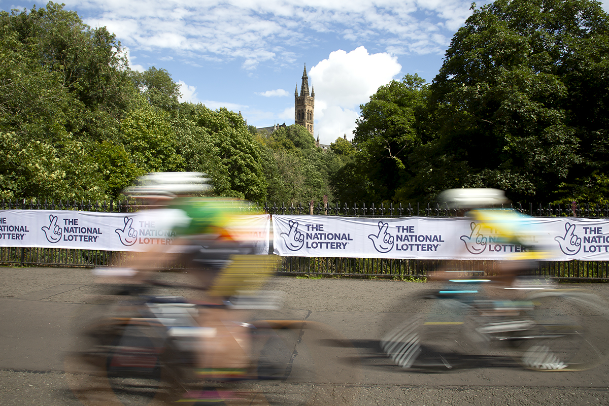 2023 UCI Cycling World Championships - Road Race - Elite Women - Riders speed past National Lottery hoardings with the South Front of the University of Glasgow in the background