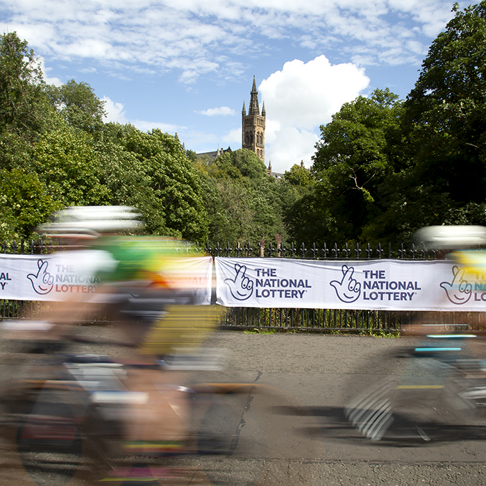 2023 UCI Cycling World Championships - Road Race - Elite Women - Riders speed past National Lottery hoardings with the South Front of the University of Glasgow in the background