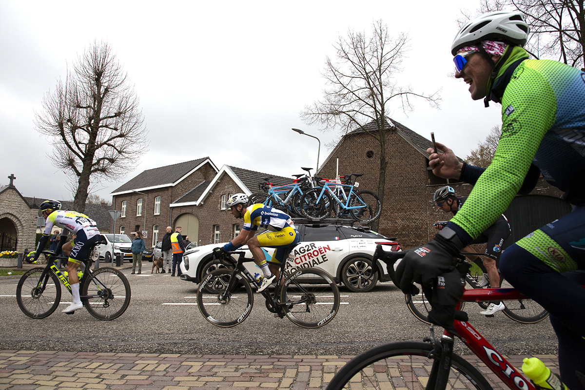 Amstel Gold Race 2023 - A fan follows the race on his bike filming on his mobile phone from the cycle path