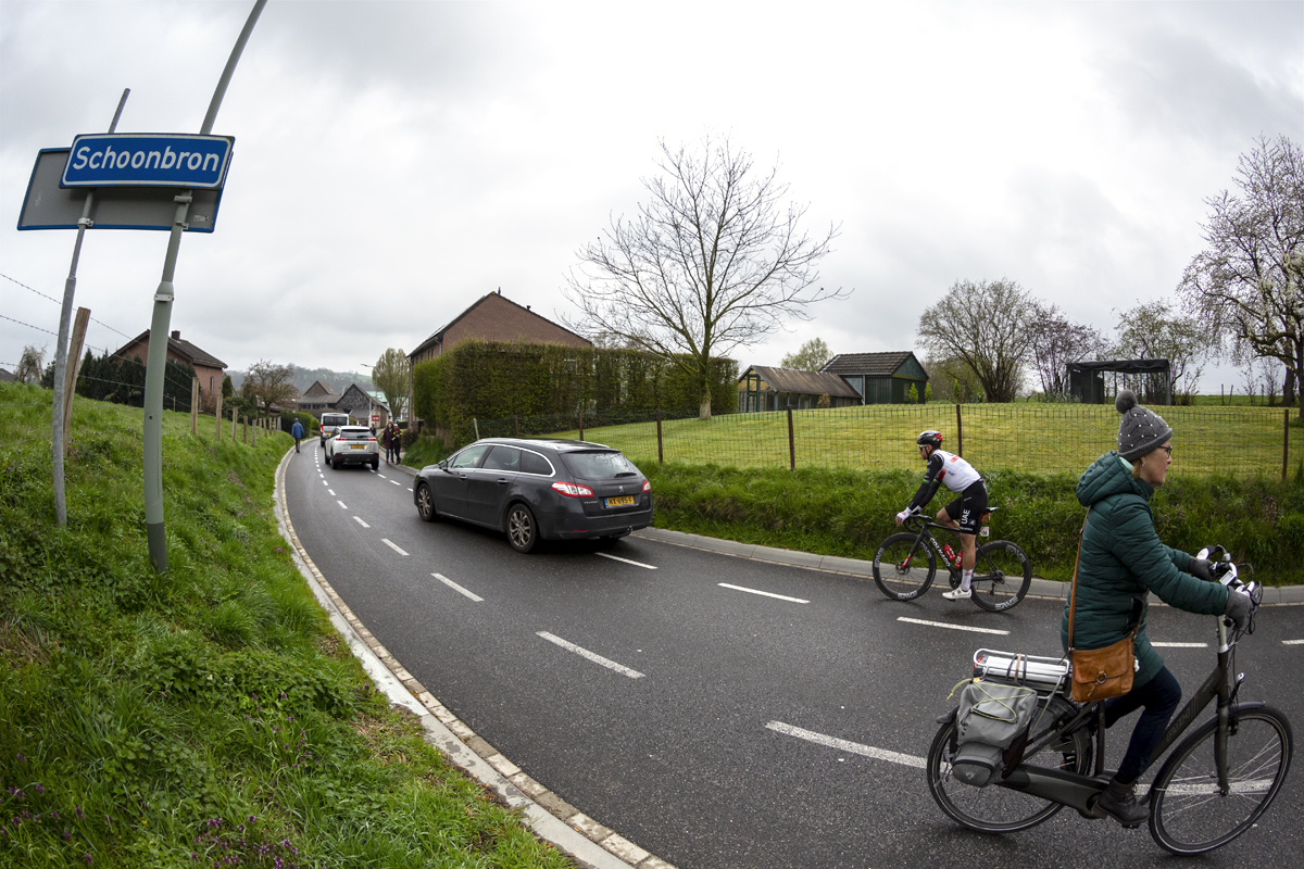 Amstel Gold Race 2023 - A woman on a bike rides on the road as a straggler from UAE Team Emirates makes their way past