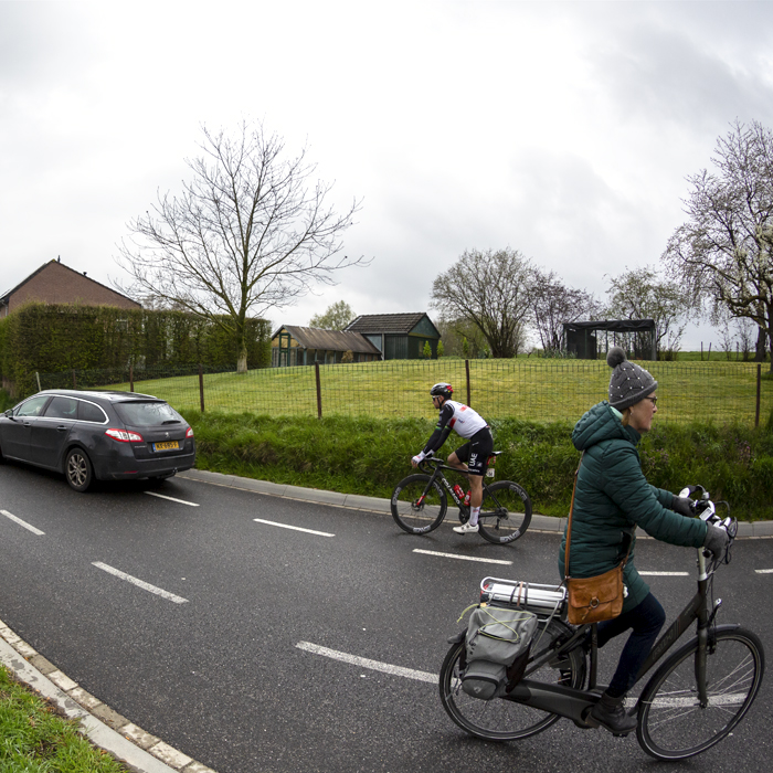 Amstel Gold Race 2023 - A woman on a bike rides on the road as a straggler from UAE Team Emirates makes their way past