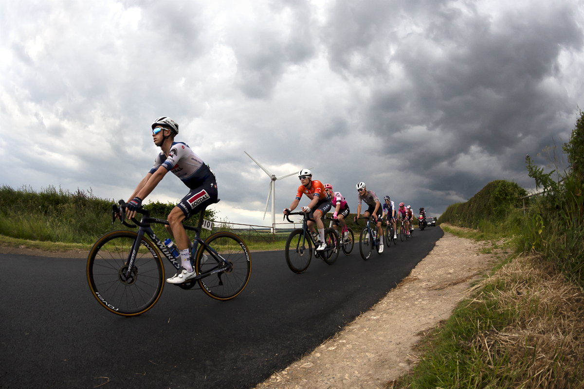 British National Road Championships 2023 - Men’s Road Race - Riders pass by a wind turbine near Brotton under stormy skies