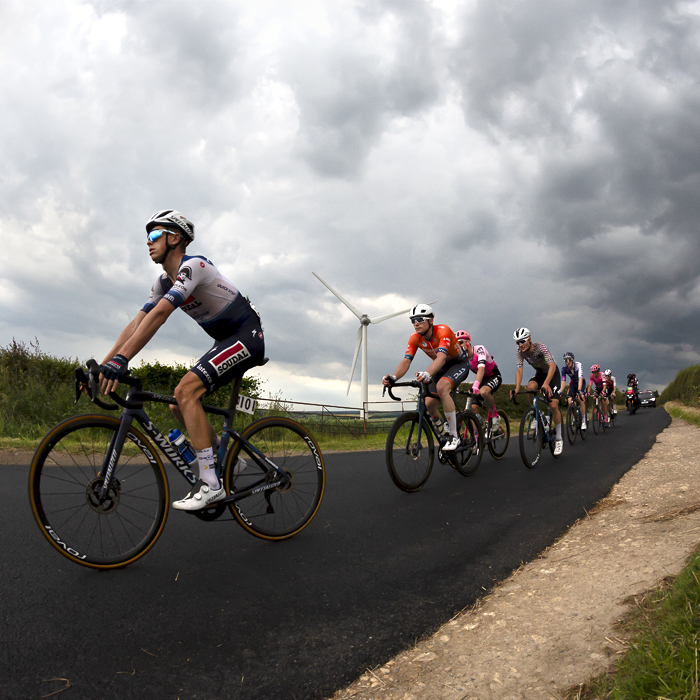 British National Road Championships 2023 - Men’s Road Race - Riders pass by a wind turbine near Brotton under stormy skies