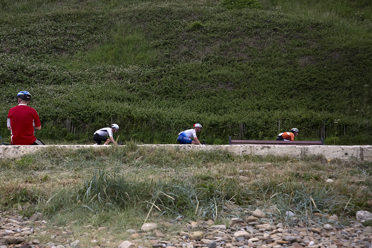 British National Road Championships 2023 - Men’s Road Race - Three riders pass a cycling fan watching from the sea wall