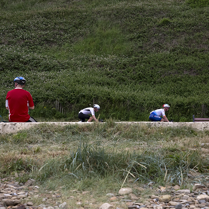 British National Road Championships 2023 - Men’s Road Race - Three riders pass a cycling fan watching from the sea wall