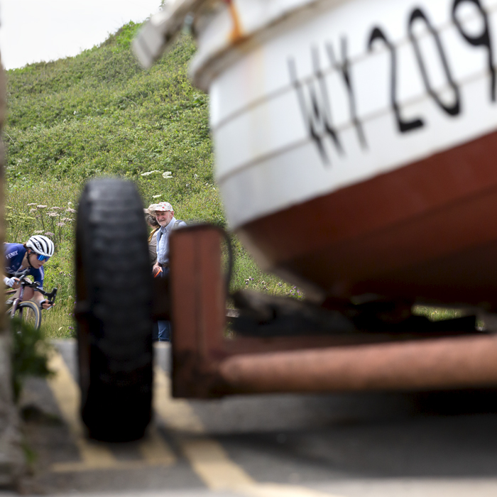 British National Road Championships 2023 - Women’s Road Race - One of the riders descends the hill framed by the fishing boat watched by an old couple