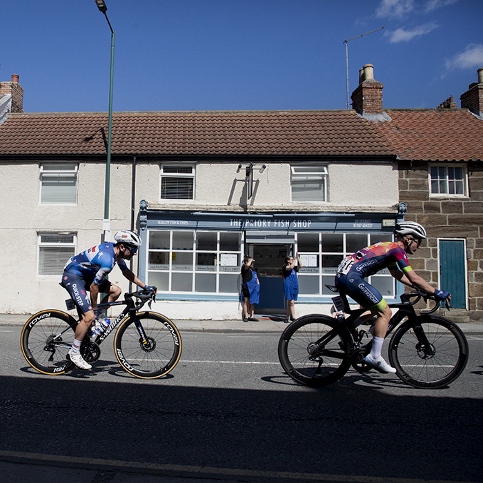 British National Road Championships 2024 - Men’s Road Race -Riders pass by a fish and chip shop as the staff watch the race