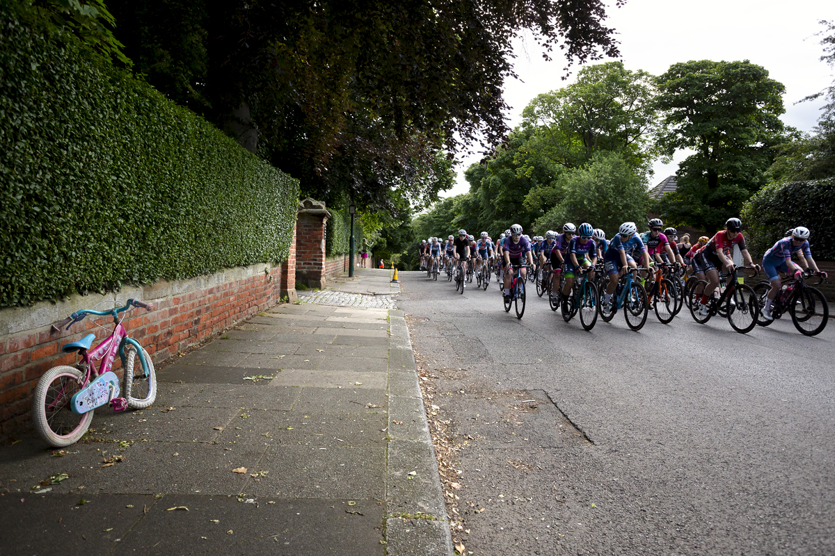 British National Road Championships 2024 - Women’s Road Race - Riders pass a broken child’s bike on the pavement as they start the race