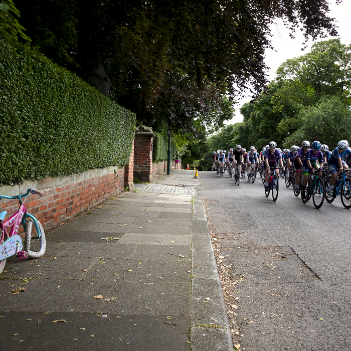 British National Road Championships 2024 - Women’s Road Race - Riders pass a broken child’s bike on the pavement as they start the race