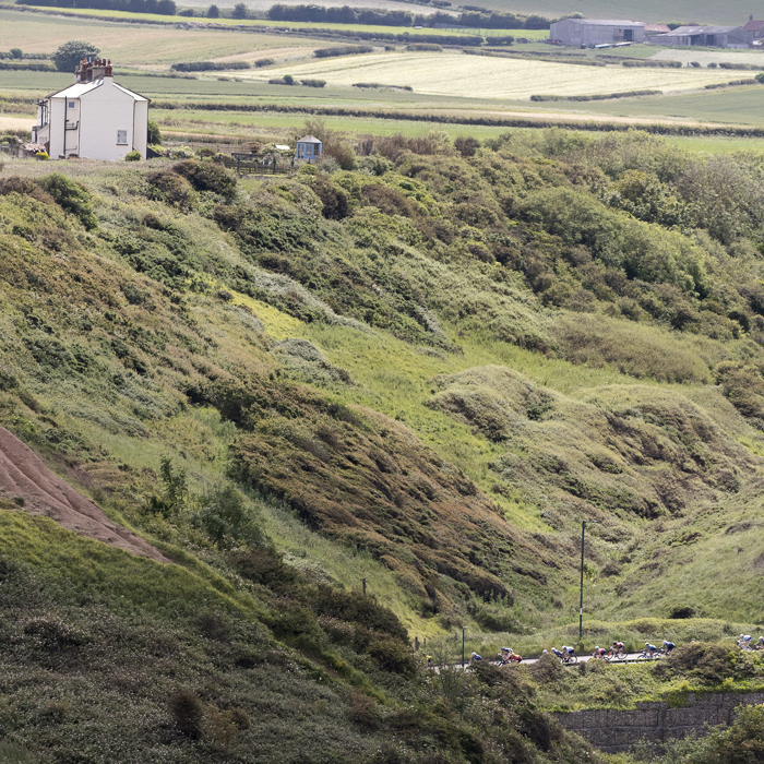 British National Road Championships 2024 - Women’s Road Race - Riders pass along the bottom of a steep sided valley with a white house on its top on the way into Saltburn