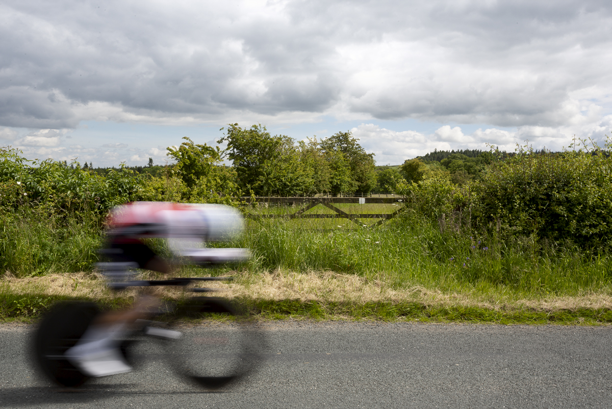 British National Road Championships 2024 - Men’s U23 Time Trial - A rider passes quickly by a five bar gate in the North Yorkshire countryside