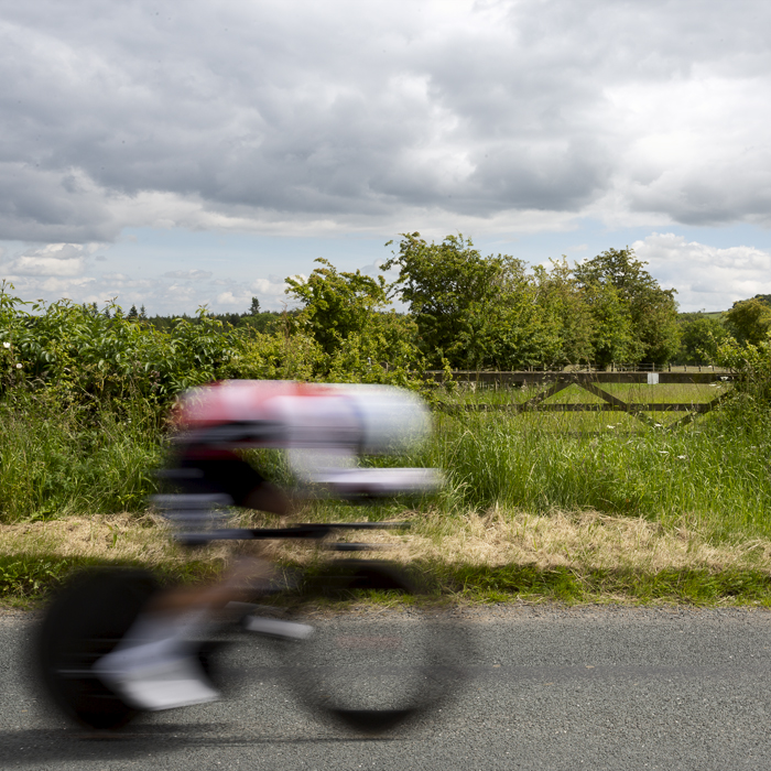 British National Road Championships 2024 - Men’s U23 Time Trial - A rider passes quickly by a five bar gate in the North Yorkshire countryside