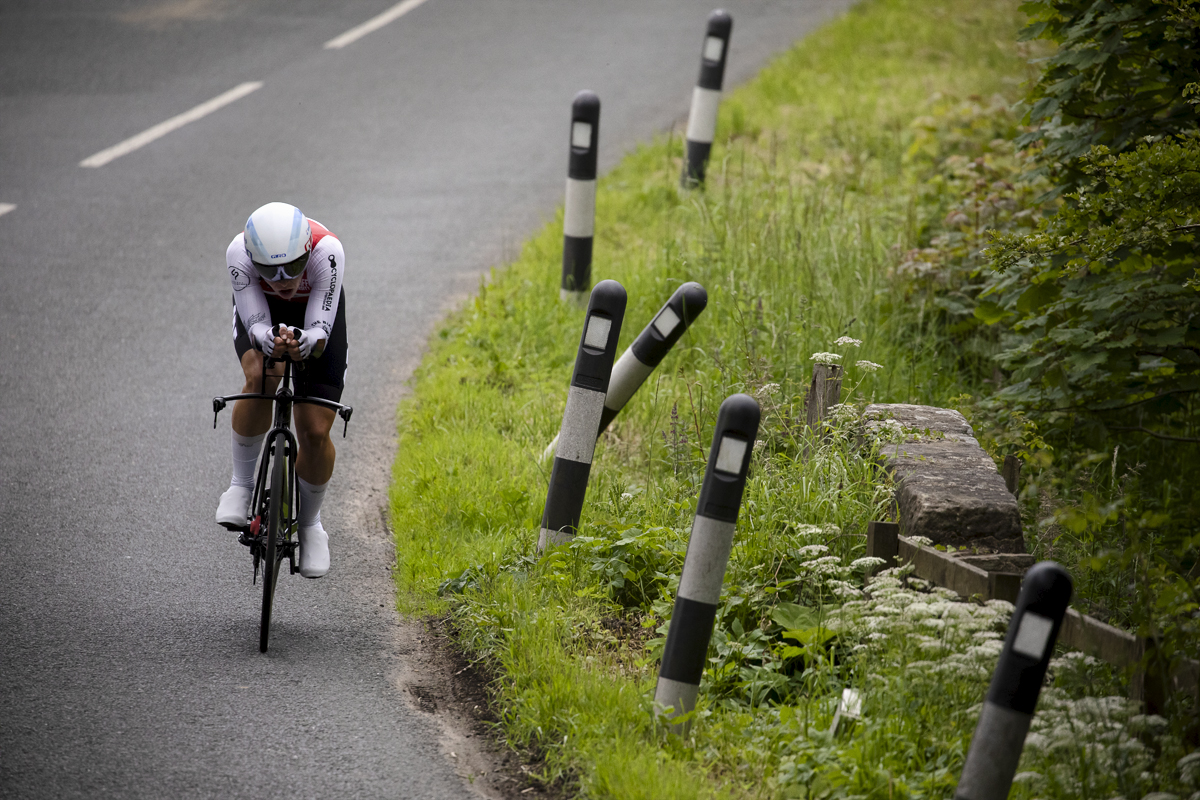 British National Road Championships 2024 - Men’s U23 Time Trial - Ollie Cadin takes a corner next to bollards in the grass at the side of the road