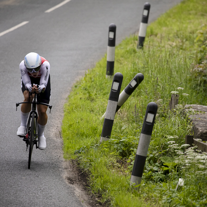 British National Road Championships 2024 - Men’s U23 Time Trial - Ollie Cadin takes a corner next to bollards in the grass at the side of the road