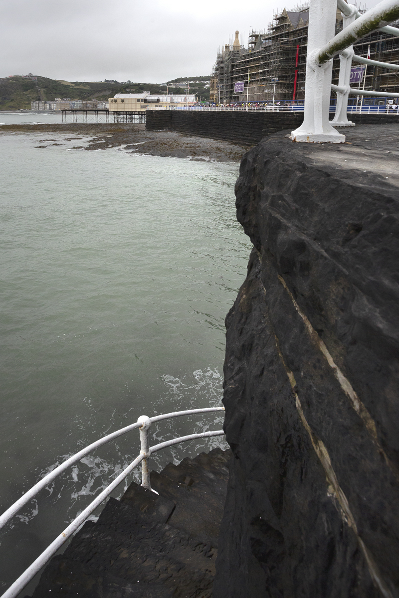 British National Road Championships 2025 - Road Race - Men - Aberystwyth - the men’s race seen from a distance with the sea in the foreground and steps leading down to the water