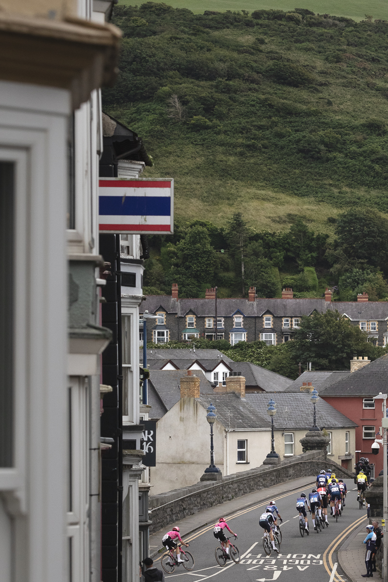 British National Road Championships 2025 - Road Race - Men - riders seen from behind as they cross a bridge in Aberystwyth