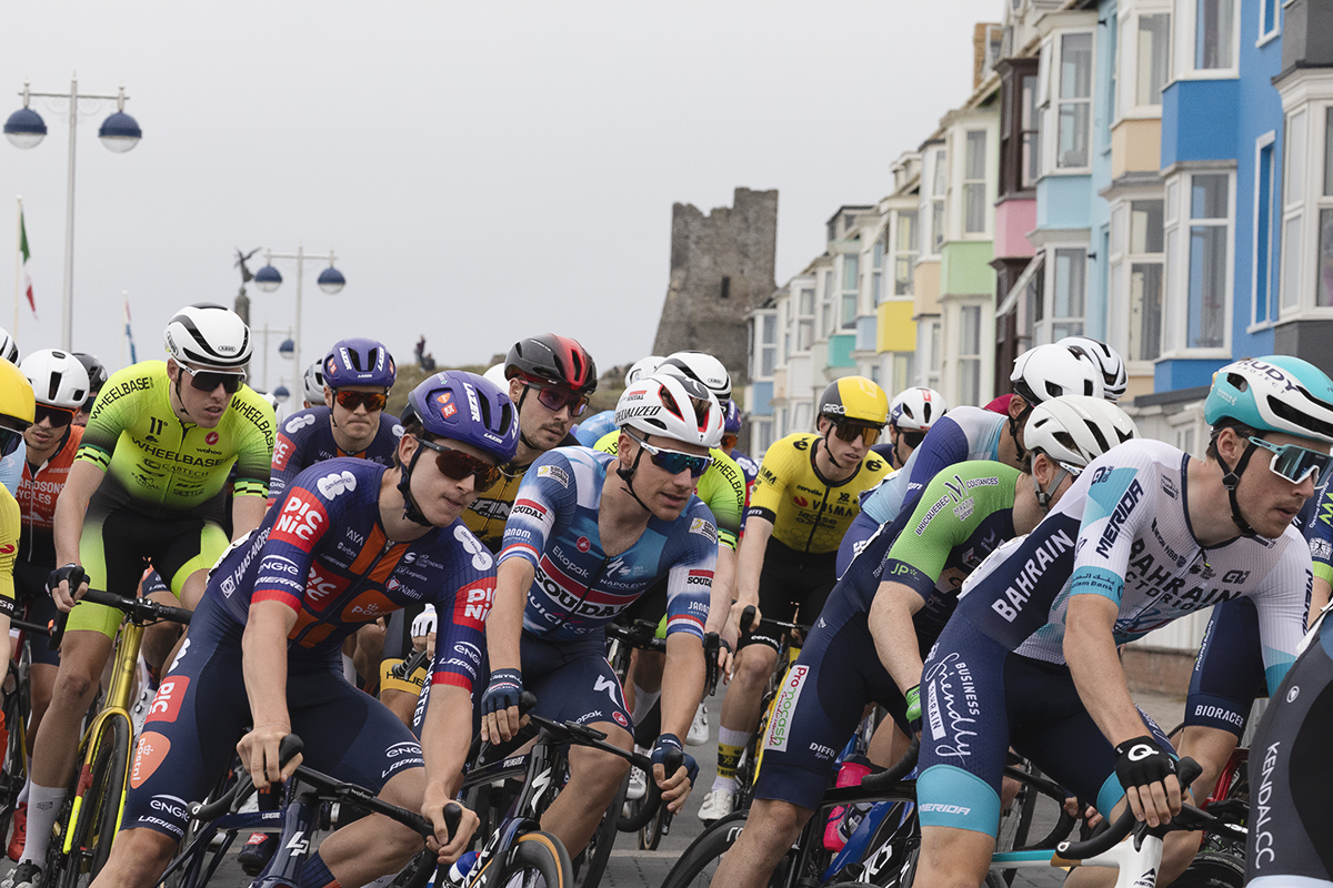 British National Road Championships 2025 - Road Race - Men - Aberystwyth - riders round a corner past brightly coloured house, castle in the background