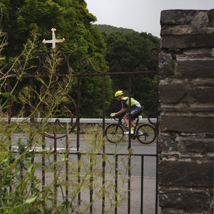 British National Road Championships 2025 - Road Race - Men - Harrison Wood of Sabgal/Anicolor seen through an iron gate with a cross on its top