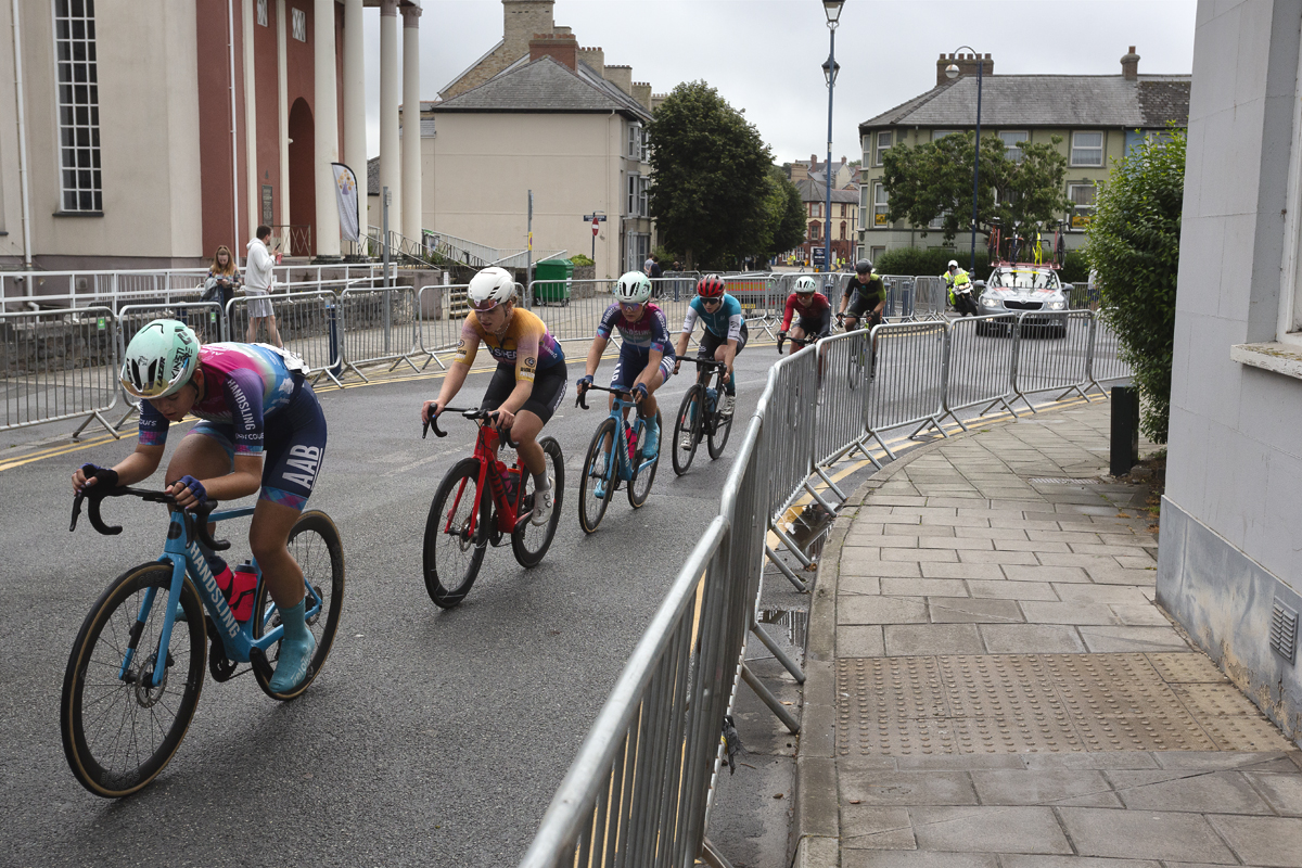 British National Road Championships 2025 - Road Race - Women - Aberystwyth - riders race through the streets past a building with columns