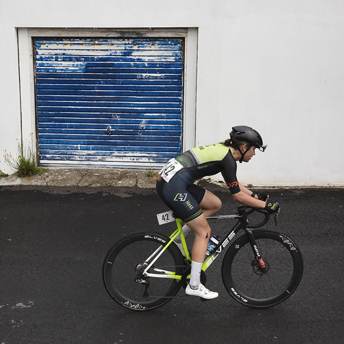 British National Road Championships 2025 - Road Race - Women - Holly Ramsey of Hess Cycling Team rides pass a tired blue garage door on a bright white garage