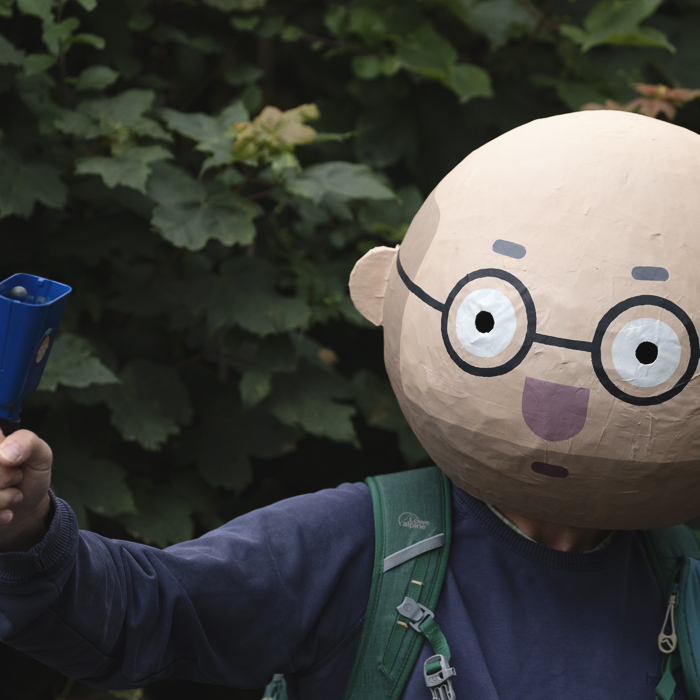 British National Road Championships 2025 - Time Trial - U23 Men - a fan wears a large Papier-mâché head and rings a cow bell to encourage riders