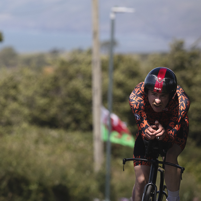 British National Road Championships 2025 - Time Trial - Elite Men - Ben Goodwin of Stolen Goat Race Team pushes up a hill while a Welsh flag flys in the background