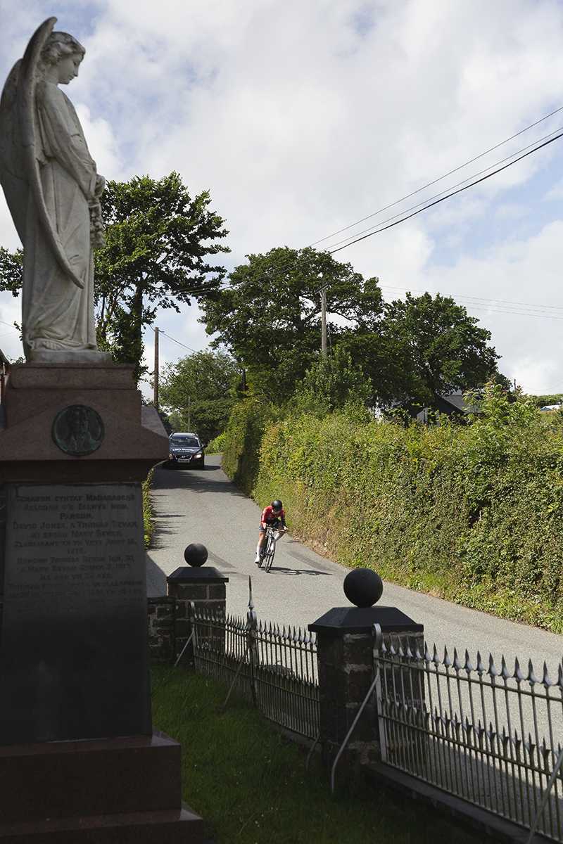 British National Road Championships 2025 - Time Trial - Elite Women - Lucy Gadd of Smurfit Westrock Cycling Team rides past a large statue of an angel in the grounds of a local chapel