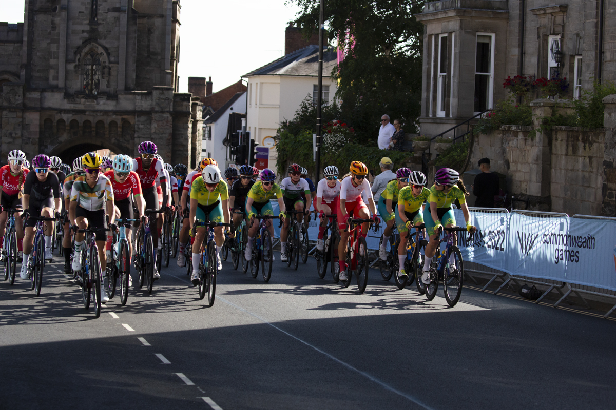 Birmingham 2022 - XXII Commonwealth Games - Women’s Road Race - the peloton races through the streets of Warwick with the East Gate in the background