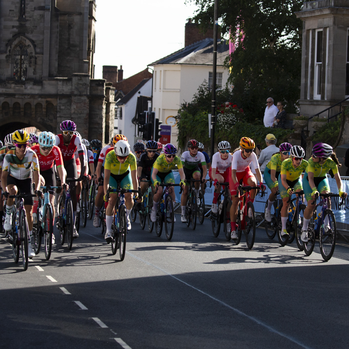 Birmingham 2022 - XXII Commonwealth Games - Women’s Road Race - the peloton races through the streets of Warwick with the East Gate in the background