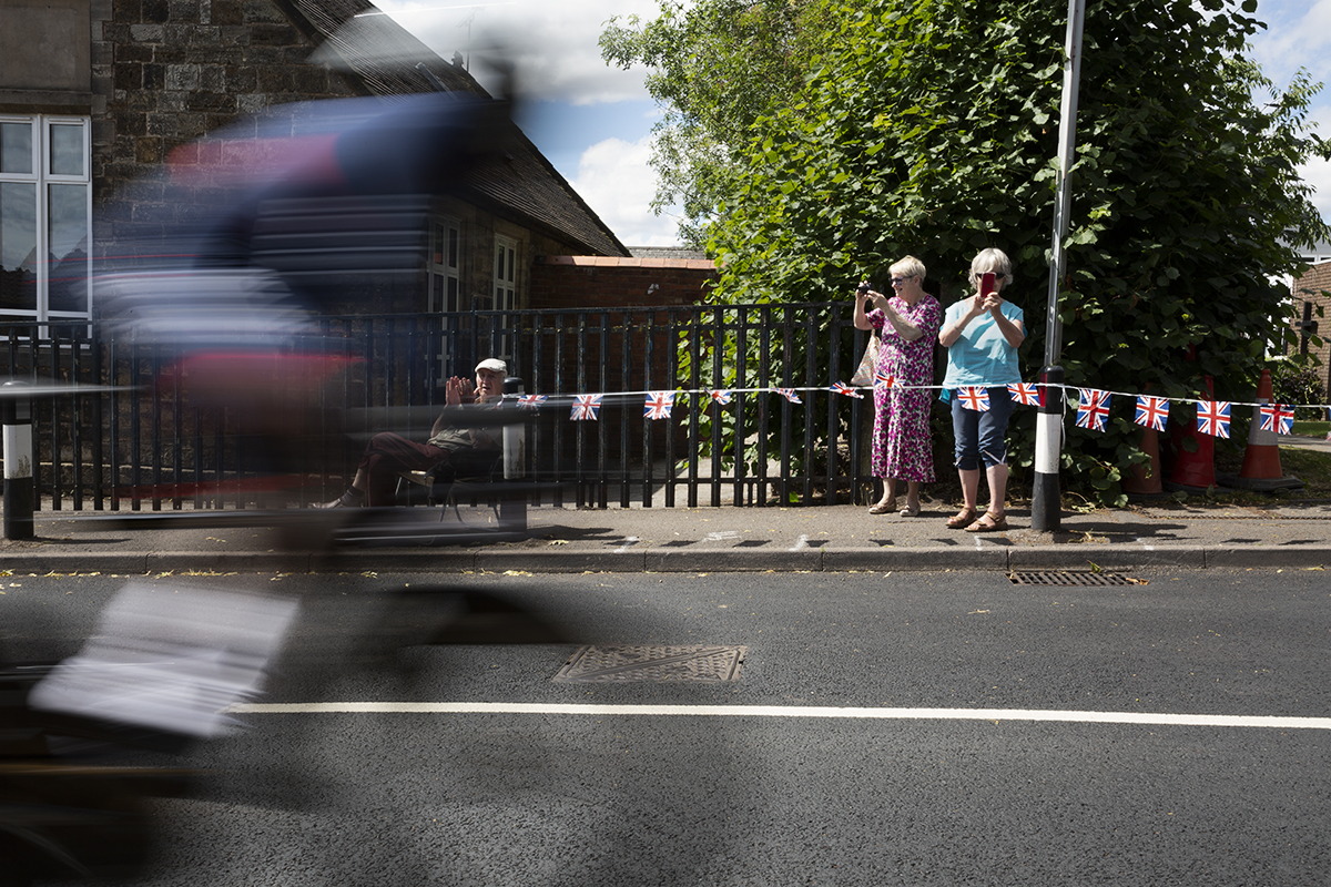 Birmingham 2022 - XXII Commonwealth Games - Men’s Time Trial - A rider from Belize passes in a blur as two older ladies clap