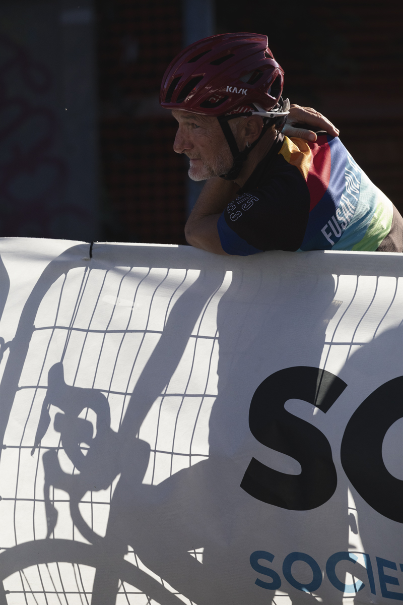 Coppa Bernocchi 2025 - A fan leans over a barrier, his bike seen as a shadow through the cloth of the hoarding