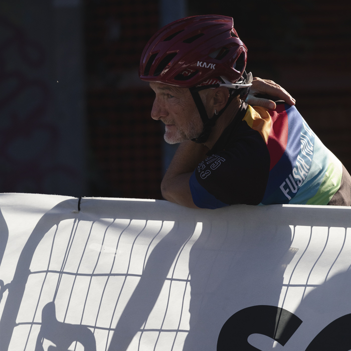 Coppa Bernocchi 2025 - A fan leans over a barrier, his bike seen as a shadow through the cloth of the hoarding