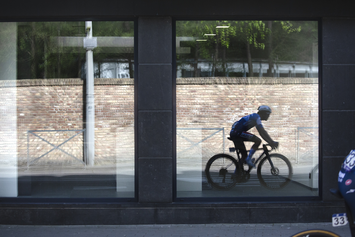 De Brabantse Pijl 2024 - Antoine Huby is reflected in a shop window whilst taking part in the race
