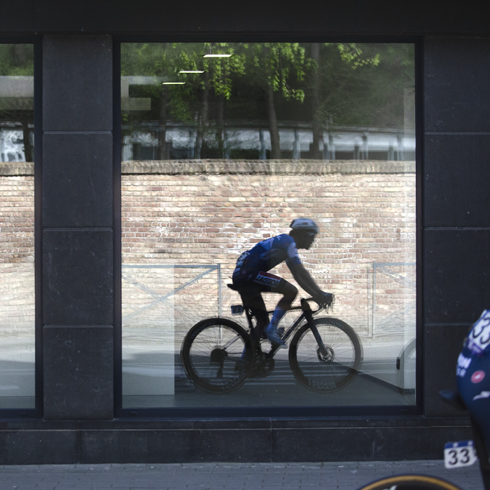 De Brabantse Pijl 2024 - Antoine Huby is reflected in a shop window whilst taking part in the race