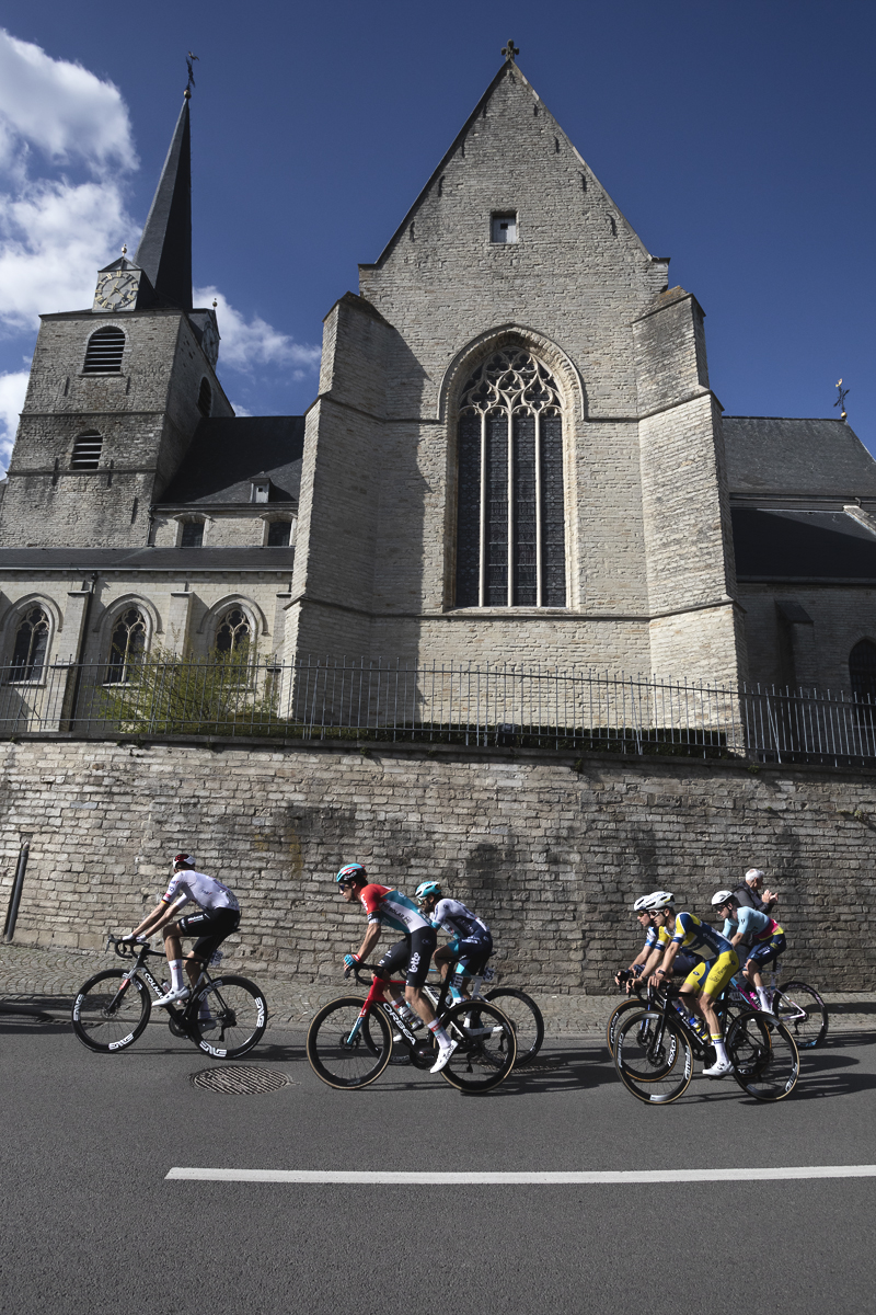 De Brabantse Pijl 2024 - A small group of riders pass Sint-Martinus Kerk which towers above the road