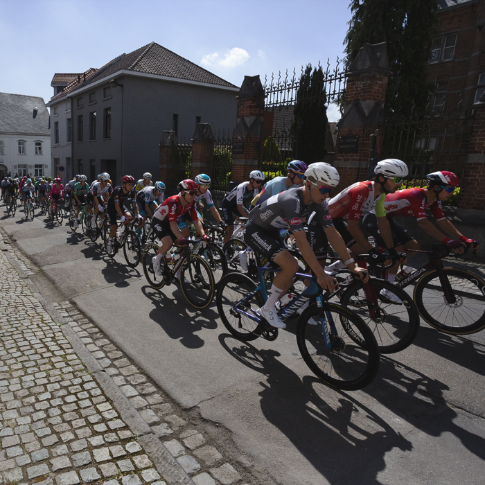 De Brabantse Pijl 2025 - Riders in Alsemberg, a cobbled path to one side and ornate gates to the other