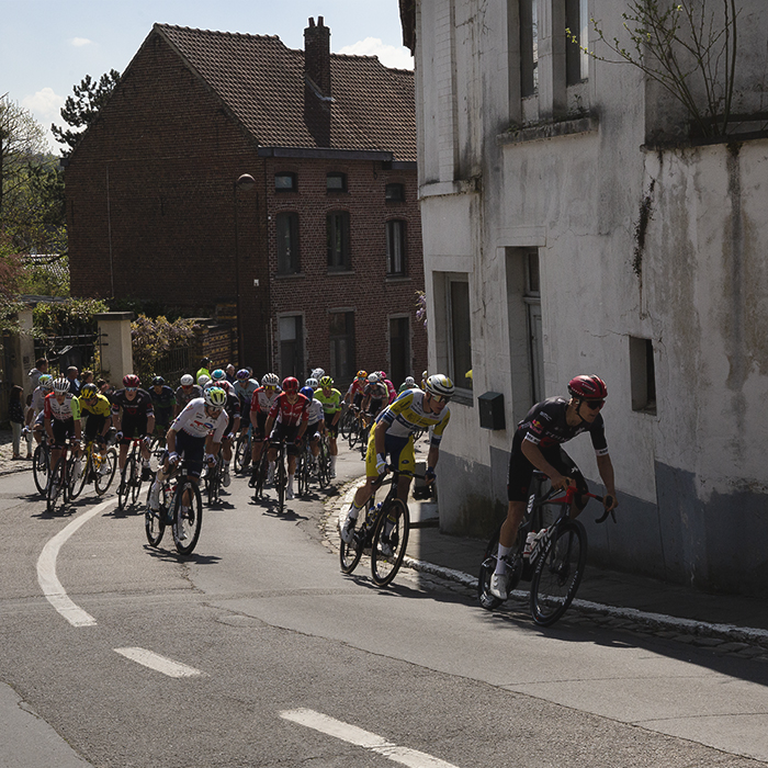 De Brabantse Pijl 2025  - A line of riders round the corner on the climb past a run down whitewashed building