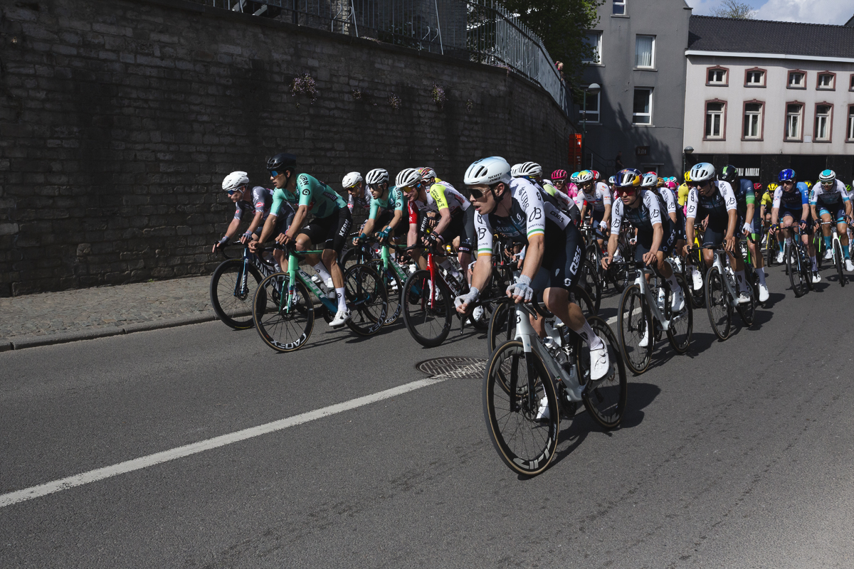 De Brabantse Pijl 2025 - The peloton passes a wall at the base of the church in Overijse