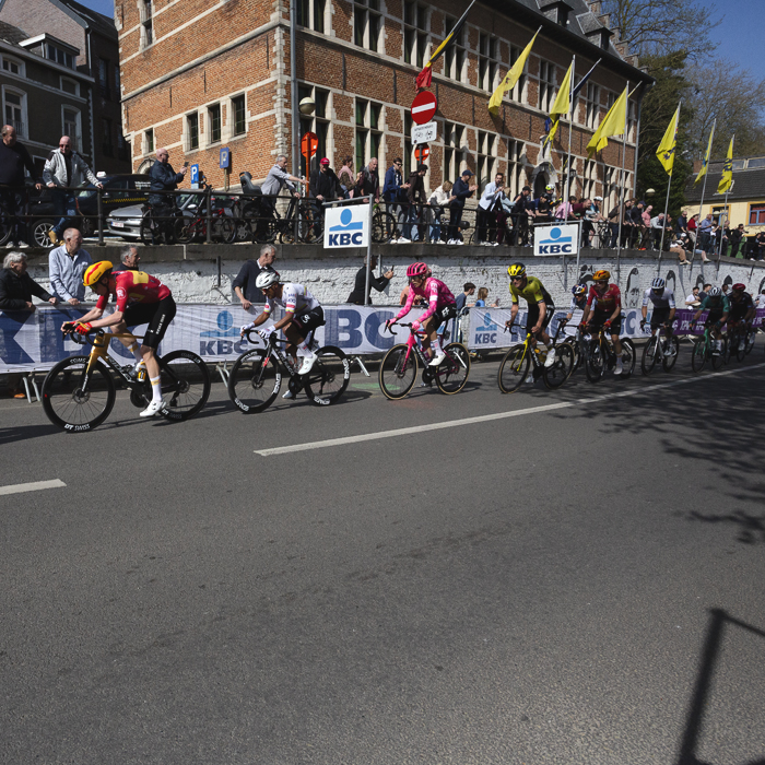 De Brabantse Pijl 2025 - A line of riders pass in front of the town hall in Overijse as fans line the streets