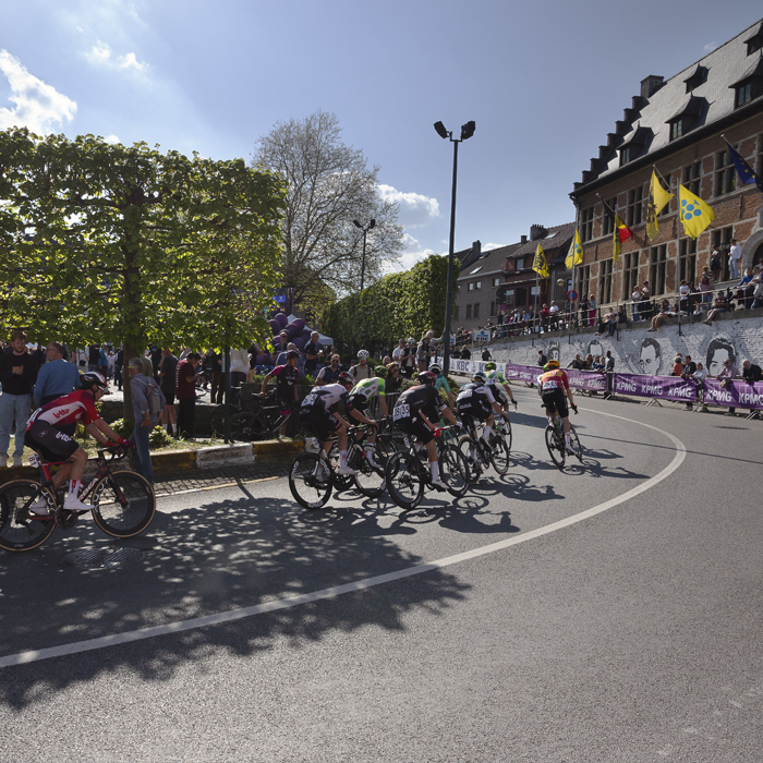 De Brabantse Pijl 2025 - Riders on the S-Bocht with the Town Hall flying flags of Flanders in the background