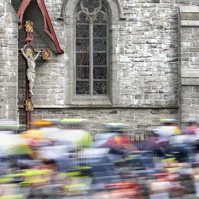 Dwars Door Vlaanderen 2022 - The peloton rushes past a church and depiction of Jesus on the cross